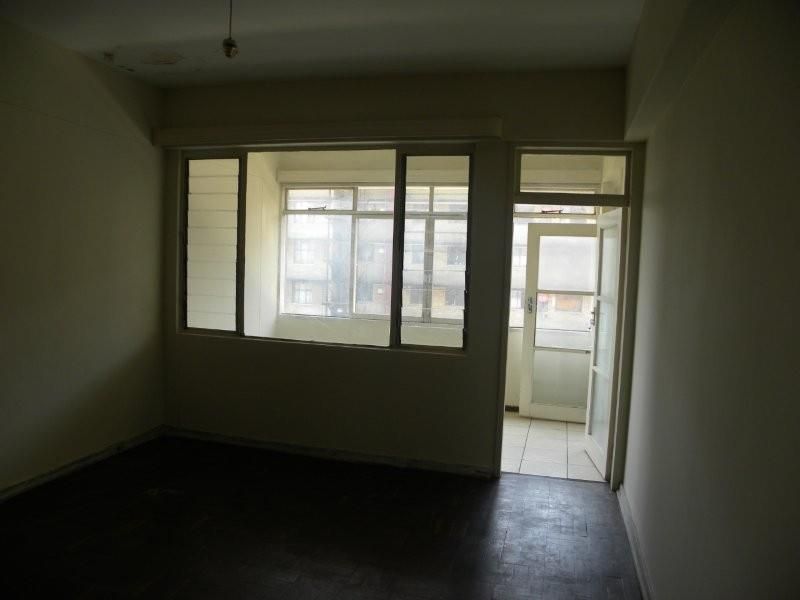 An empty living room featuring parquet flooring, large windows, and direct access to an adjoining balcony area.