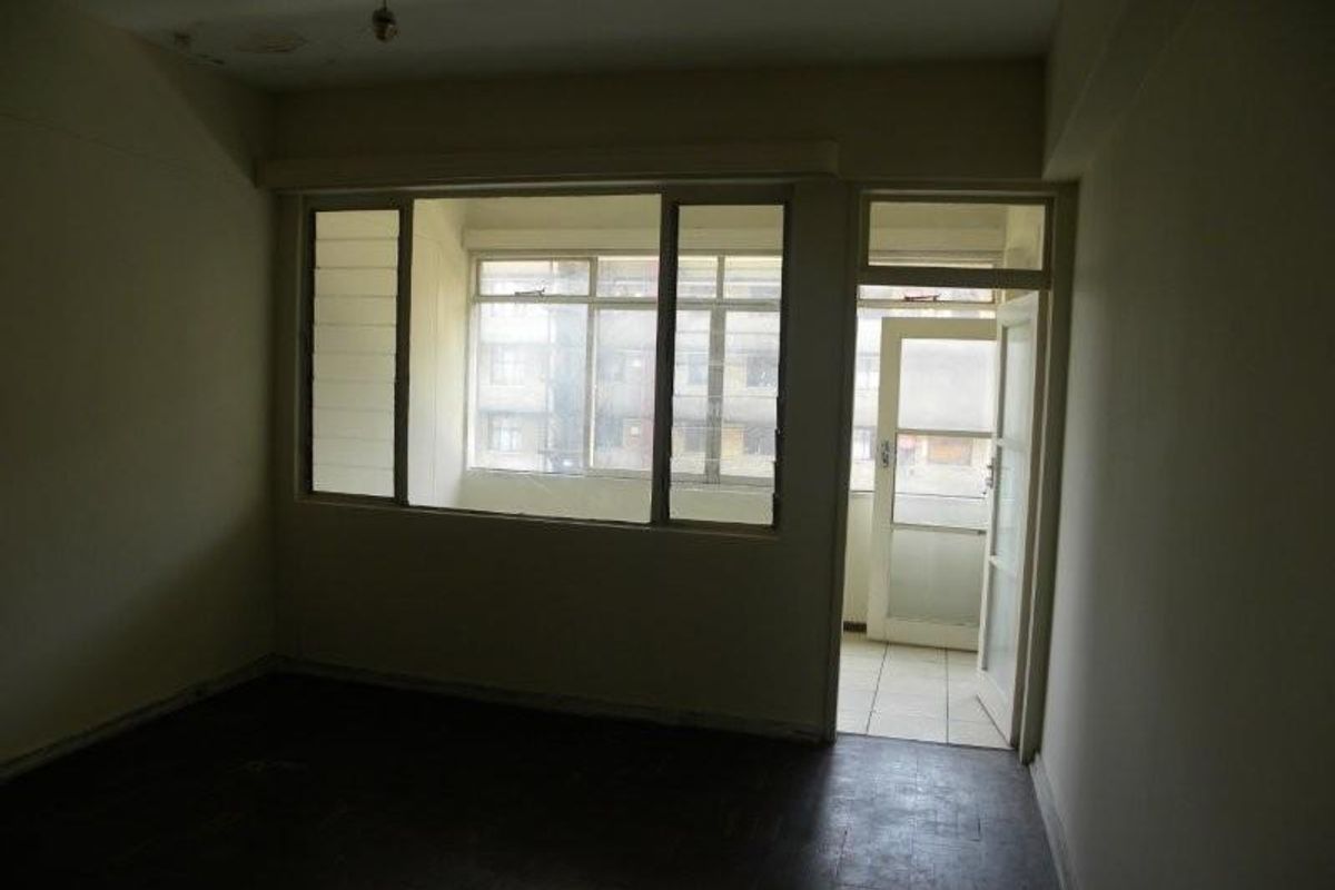An empty living room featuring parquet flooring, large windows, and direct access to an adjoining balcony area.