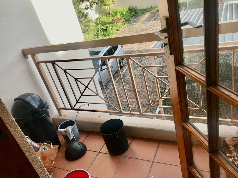 A small balcony featuring tiled flooring and a metal balustrade, accessible through a timber-framed glass door.