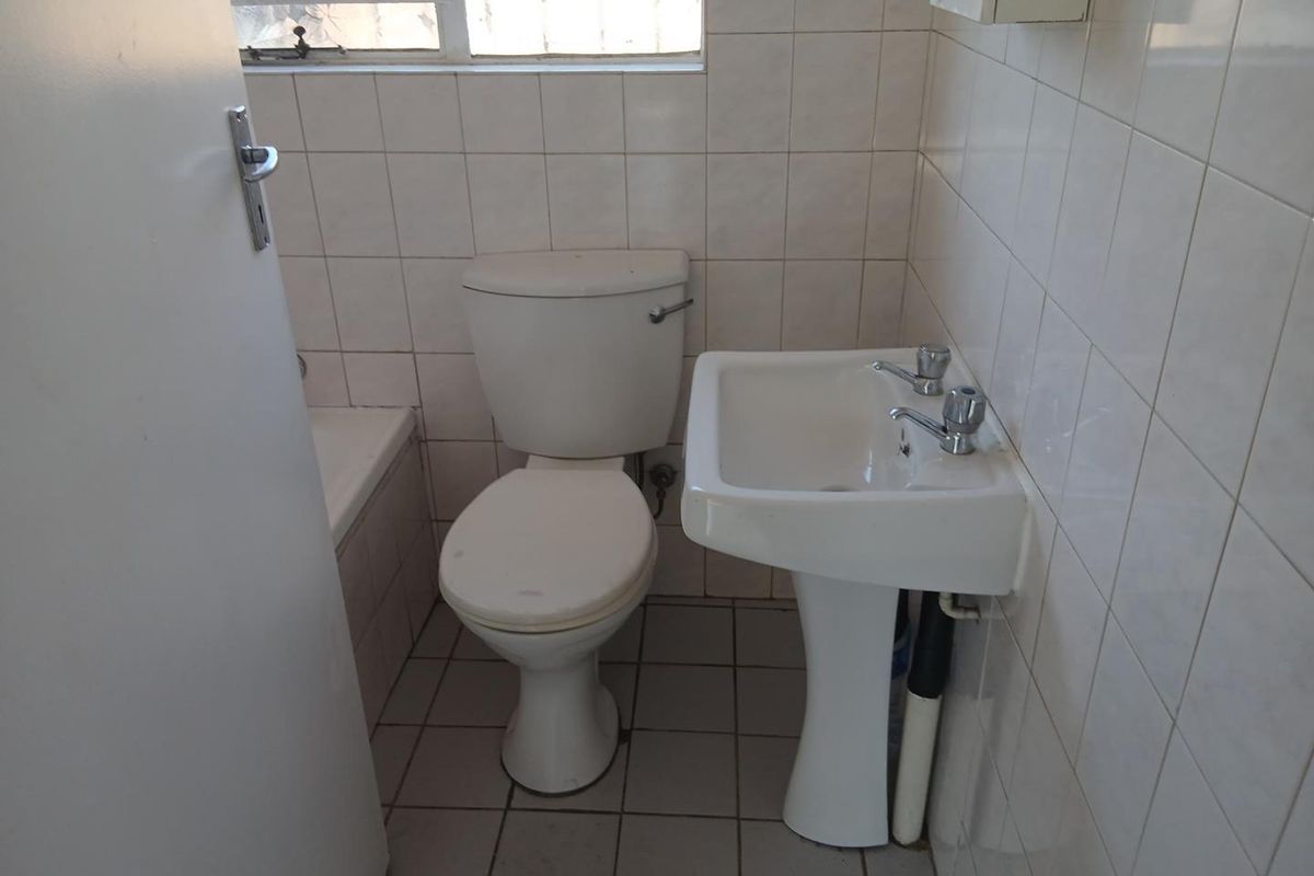 A compact bathroom featuring a pedestal basin, toilet, and bathtub with dated ceramic wall and floor tiling.