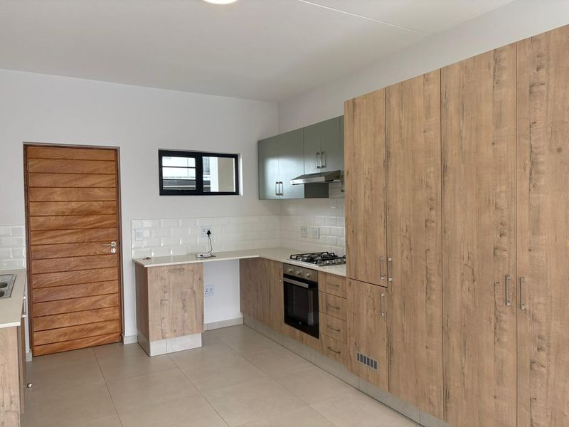 Modern kitchen featuring wood-grain cabinetry, stone countertops, subway tile backsplash, and integrated gas hob with oven.
