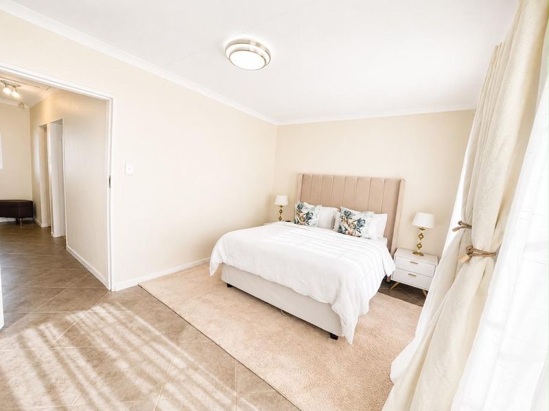 A well-maintained bedroom featuring neutral wall tones, tiled flooring, and a clean, bright aesthetic with direct access to the hallway.