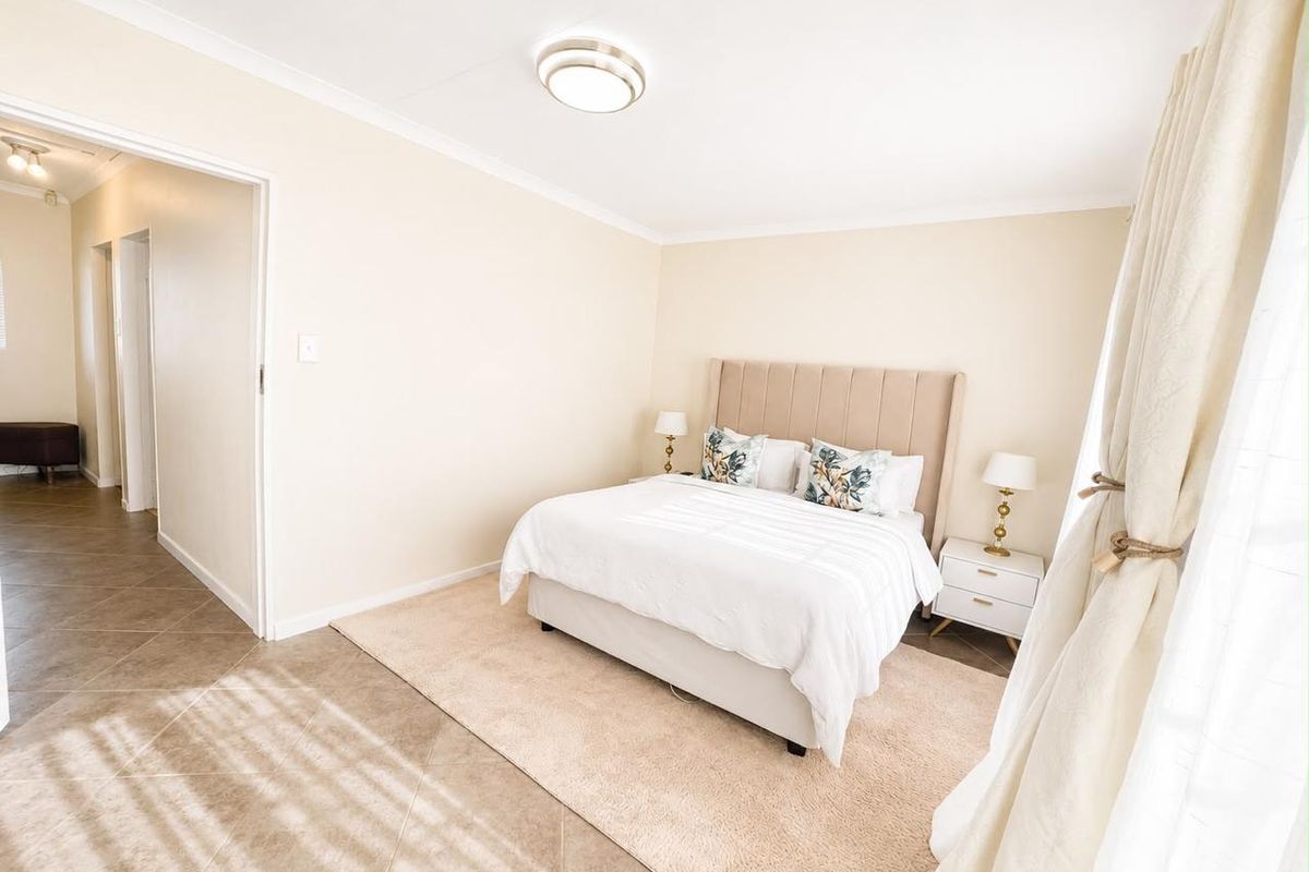 A well-maintained bedroom featuring neutral wall tones, tiled flooring, and a clean, bright aesthetic with direct access to the hallway.