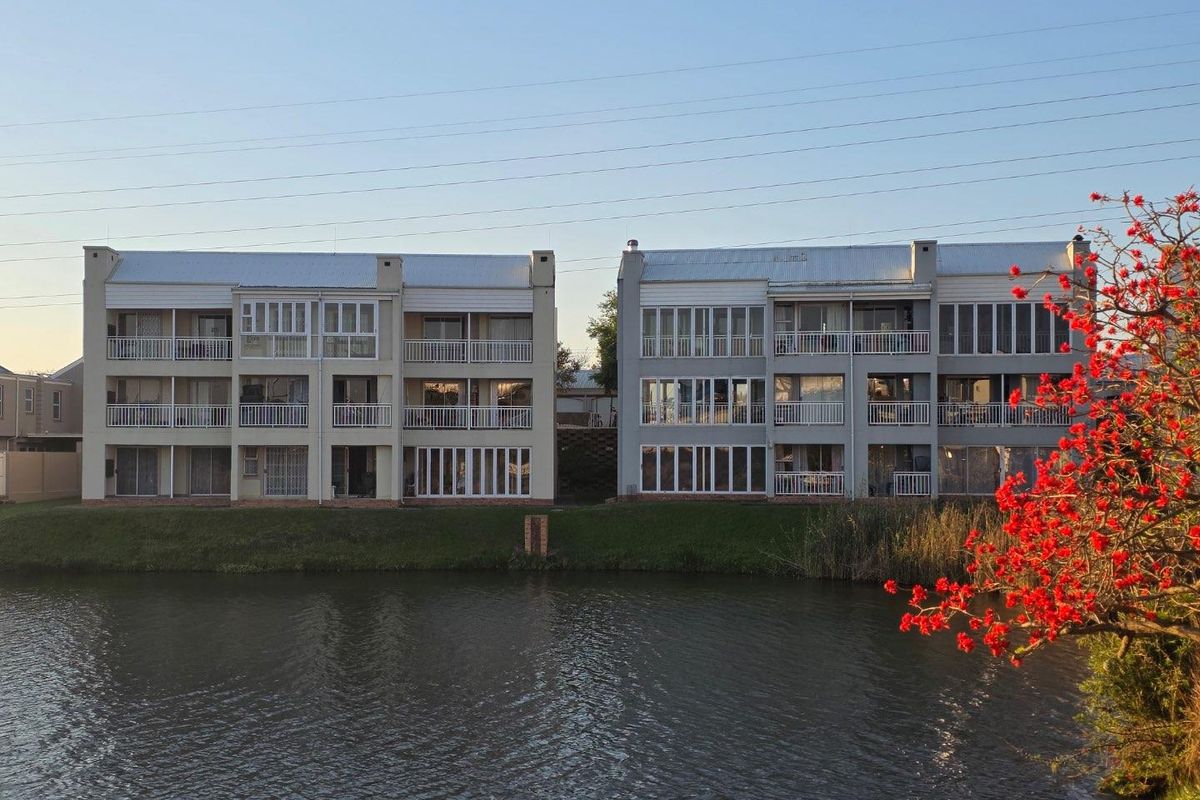 A view of the rear facade of a multi-story apartment complex featuring balconies and sliding glass doors overlooking a waterfront area.