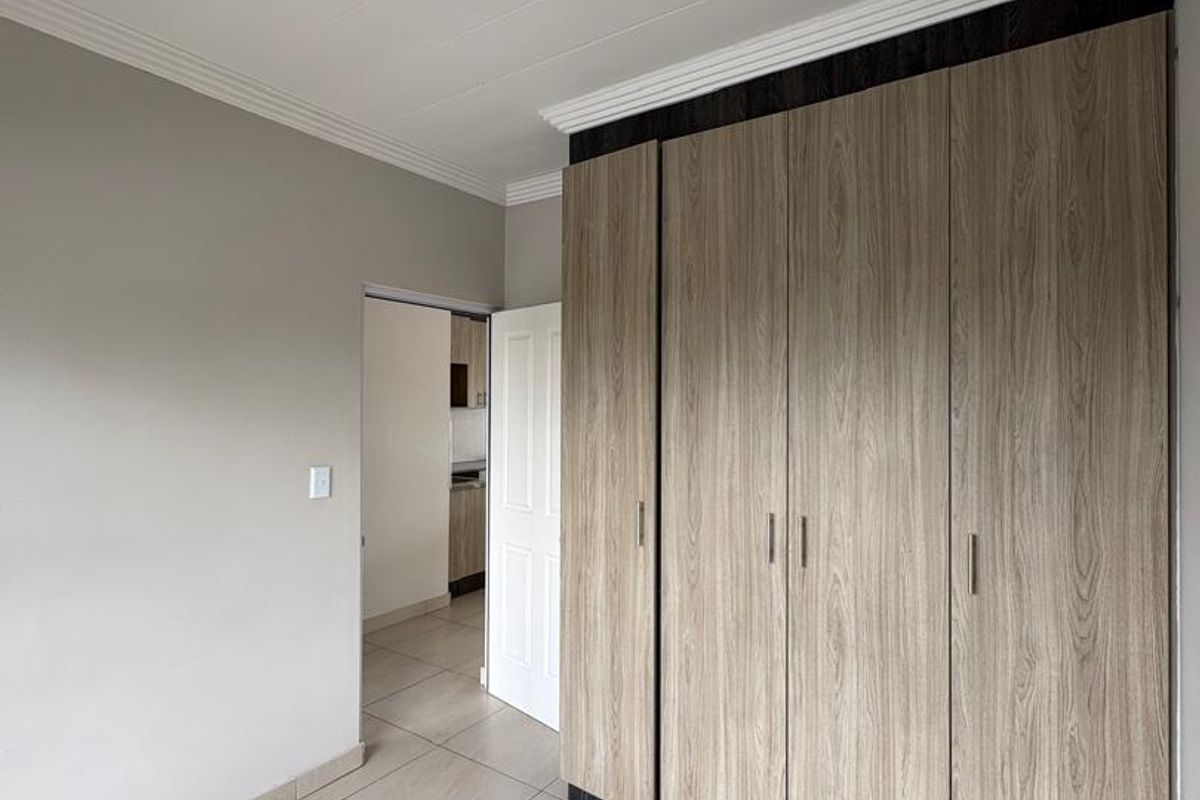 A bright bedroom featuring neutral tiled flooring, modern wood-grain built-in cupboards, and a clean, minimalist aesthetic.