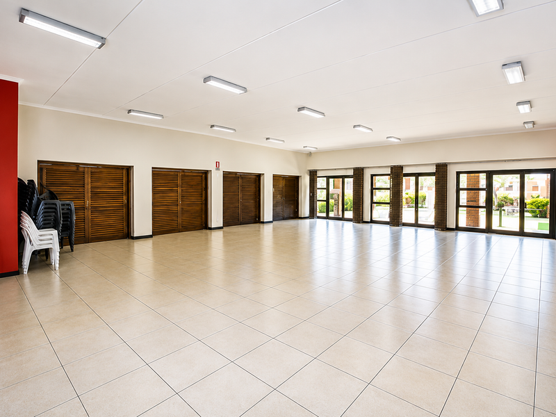 A spacious, open-plan clubhouse area featuring neutral tiled flooring, multiple glass access doors, and functional overhead lighting, suitable for events or communal use.
