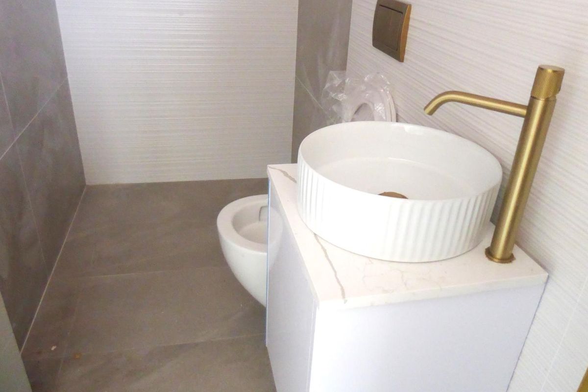 Modern bathroom featuring a contemporary vessel sink with brass faucet, stone-topped vanity, and neutral wall and floor tiling.