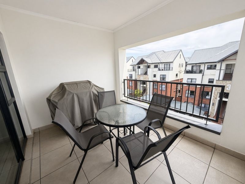 A covered balcony featuring tiled flooring and a metal balustrade, offering an outdoor space with views of the surrounding apartment complex.