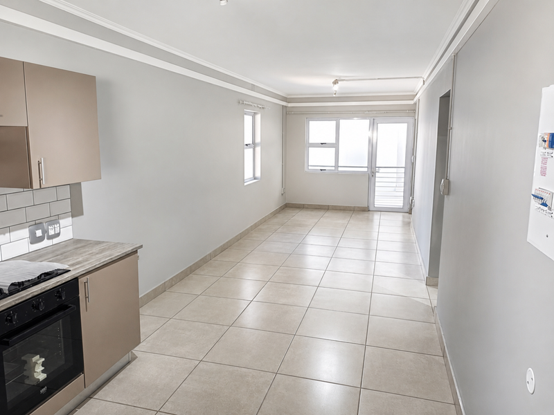 An open-plan kitchen and living area featuring neutral tiled flooring, modern cabinetry, built-in oven, and direct access to an outdoor space via a sliding door.