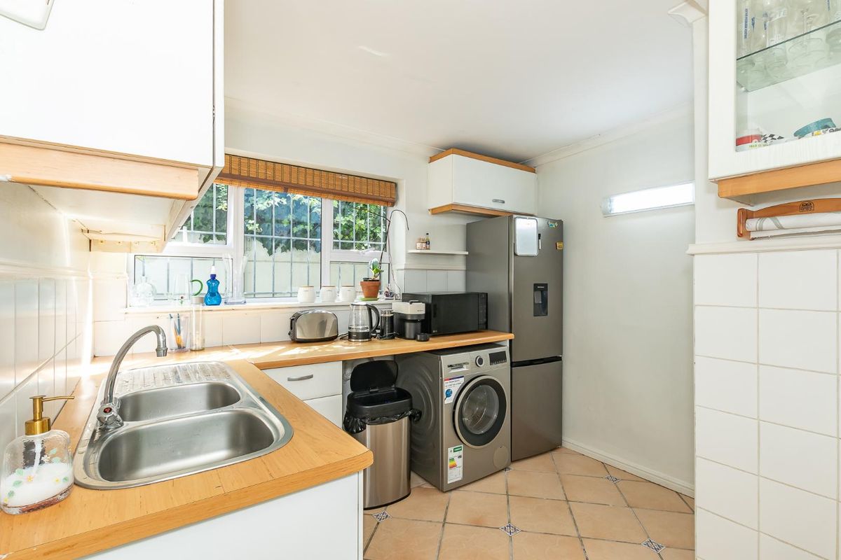 A functional kitchen featuring a double stainless steel sink, wooden countertops, tiled flooring, and space for integrated laundry appliances.