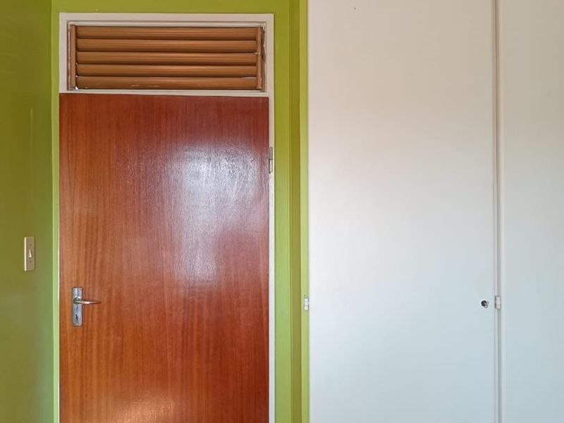A bedroom interior featuring a built-in wardrobe, a wooden door with a louvered transom window, and lime green painted walls.