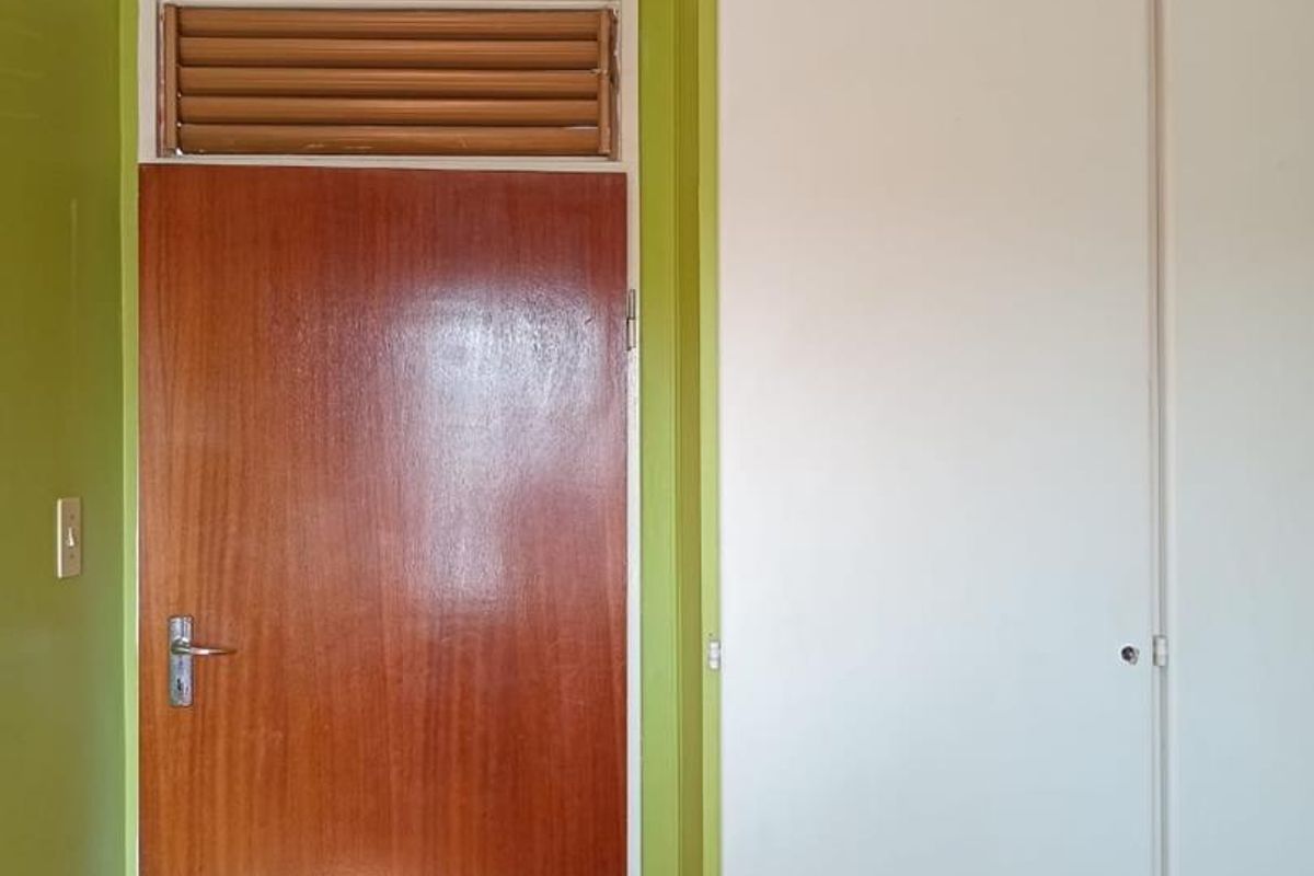 A bedroom interior featuring a built-in wardrobe, a wooden door with a louvered transom window, and lime green painted walls.