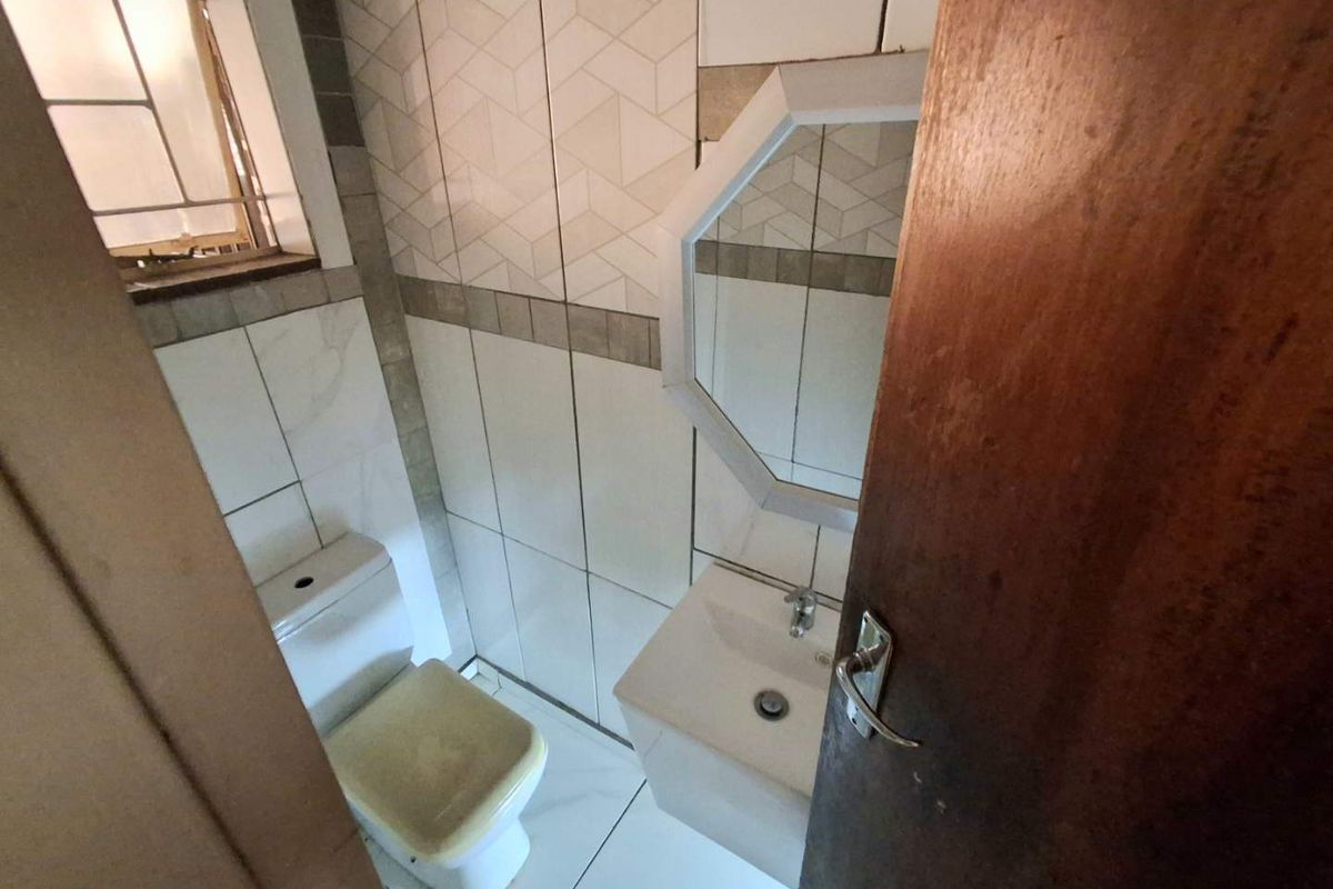 Compact bathroom featuring tiled walls, a wall-mounted basin, and a standard toilet, providing a functional space with neutral finishes.
