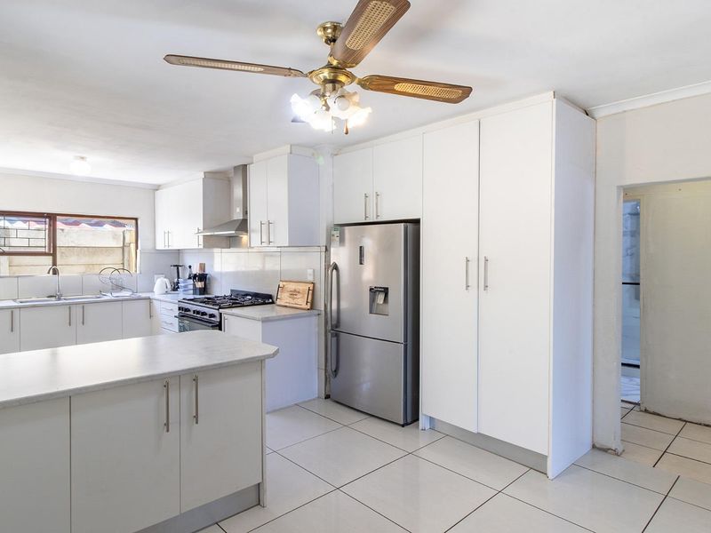A bright, functional kitchen featuring white cabinetry, a central island, gas hob with extractor, and tiled flooring throughout.
