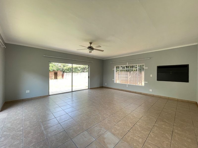 Spacious, light-filled living area featuring neutral tiled flooring, a ceiling fan, and large sliding doors providing direct access to the rear garden.