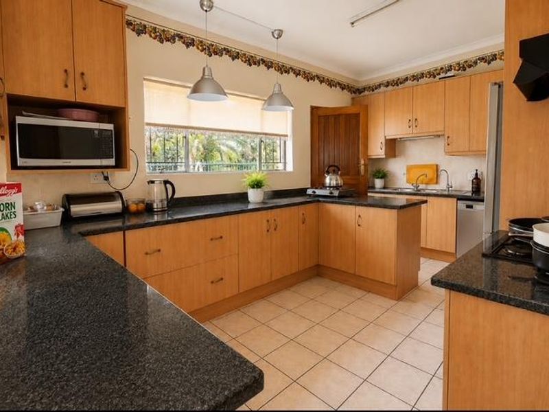 A functional kitchen featuring light wood cabinetry, dark granite countertops, tiled flooring, and ample workspace with integrated appliances.