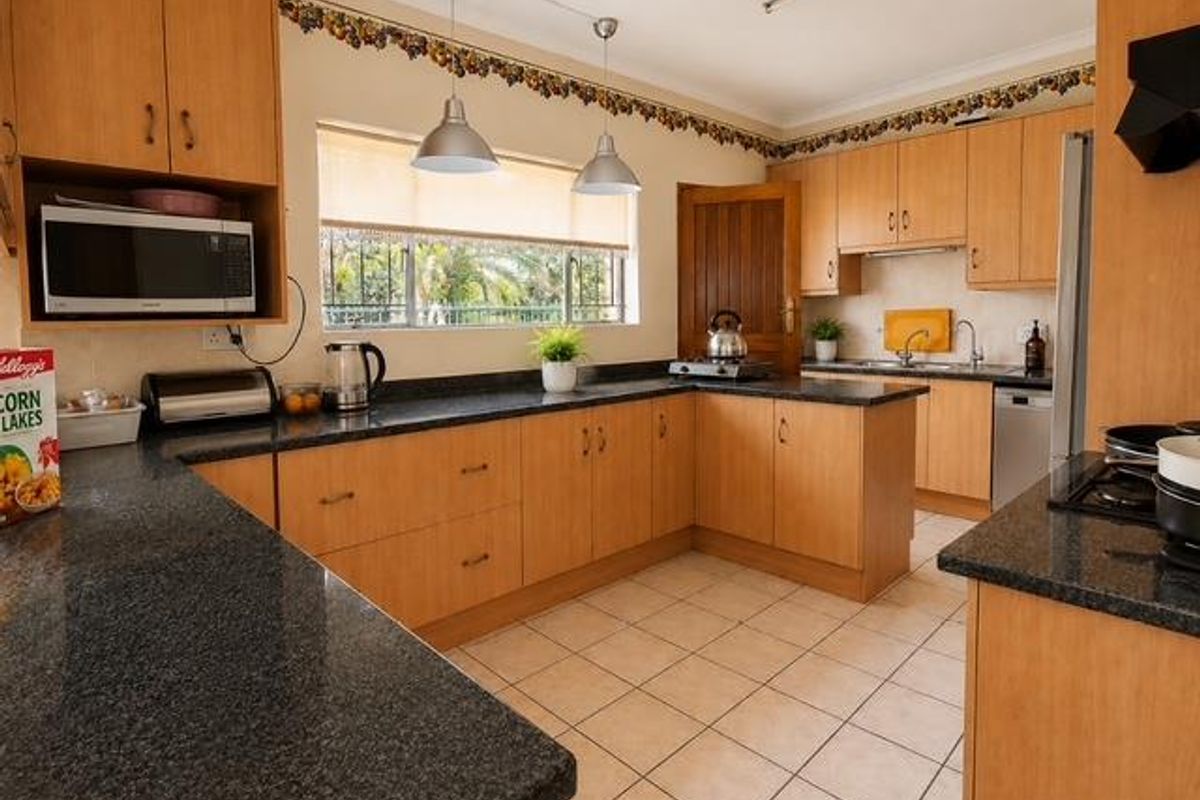 A functional kitchen featuring light wood cabinetry, dark granite countertops, tiled flooring, and ample workspace with integrated appliances.
