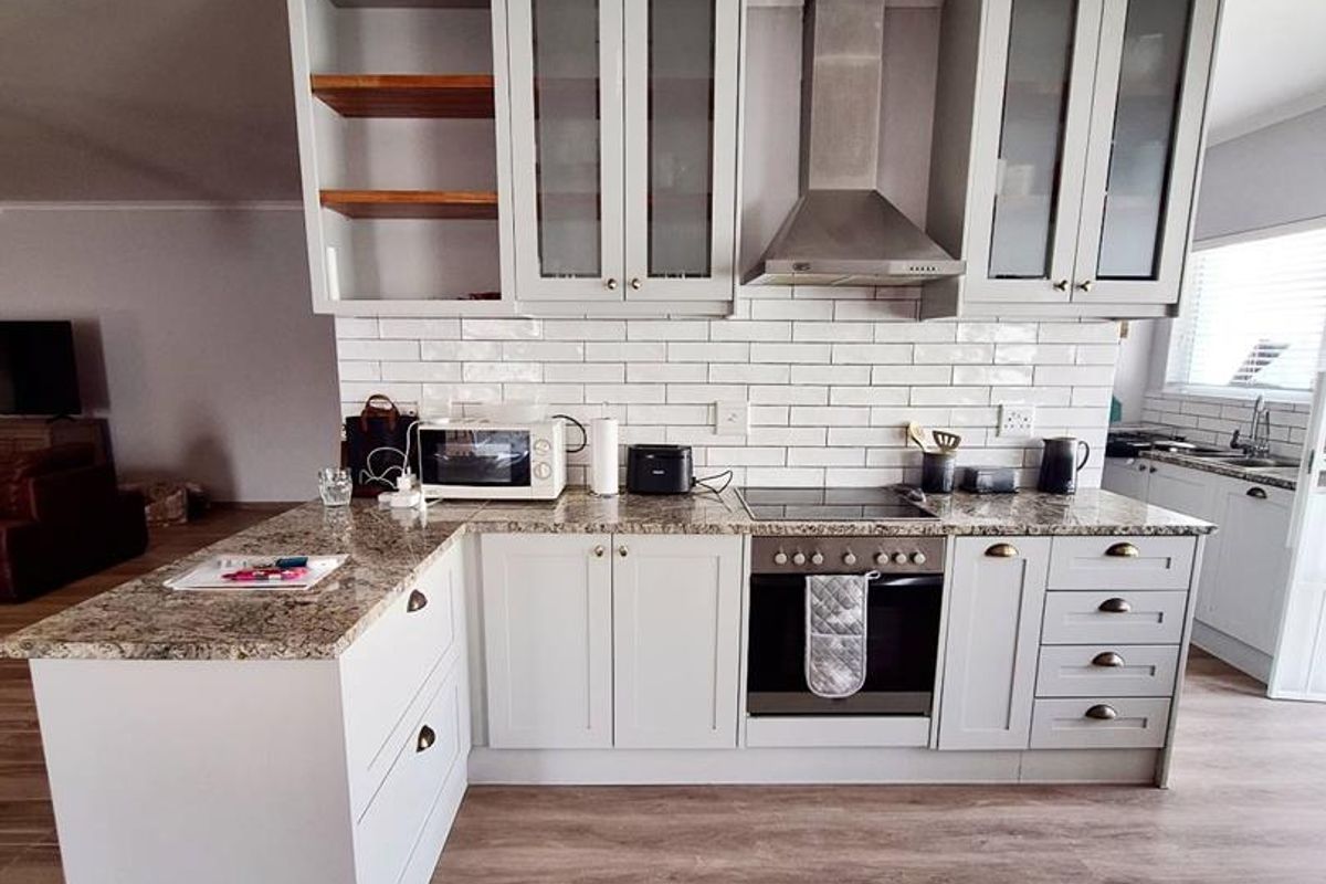 Modern kitchen featuring light grey cabinetry, granite countertops, subway tile backsplash, stainless steel extractor fan, and integrated oven with wood-look flooring.
