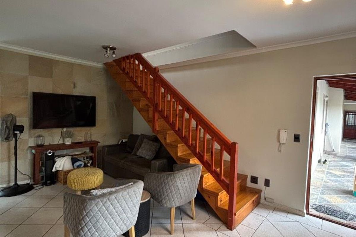 Open plan living area featuring tiled flooring, a stone feature wall, and a wooden staircase leading to the upper level.