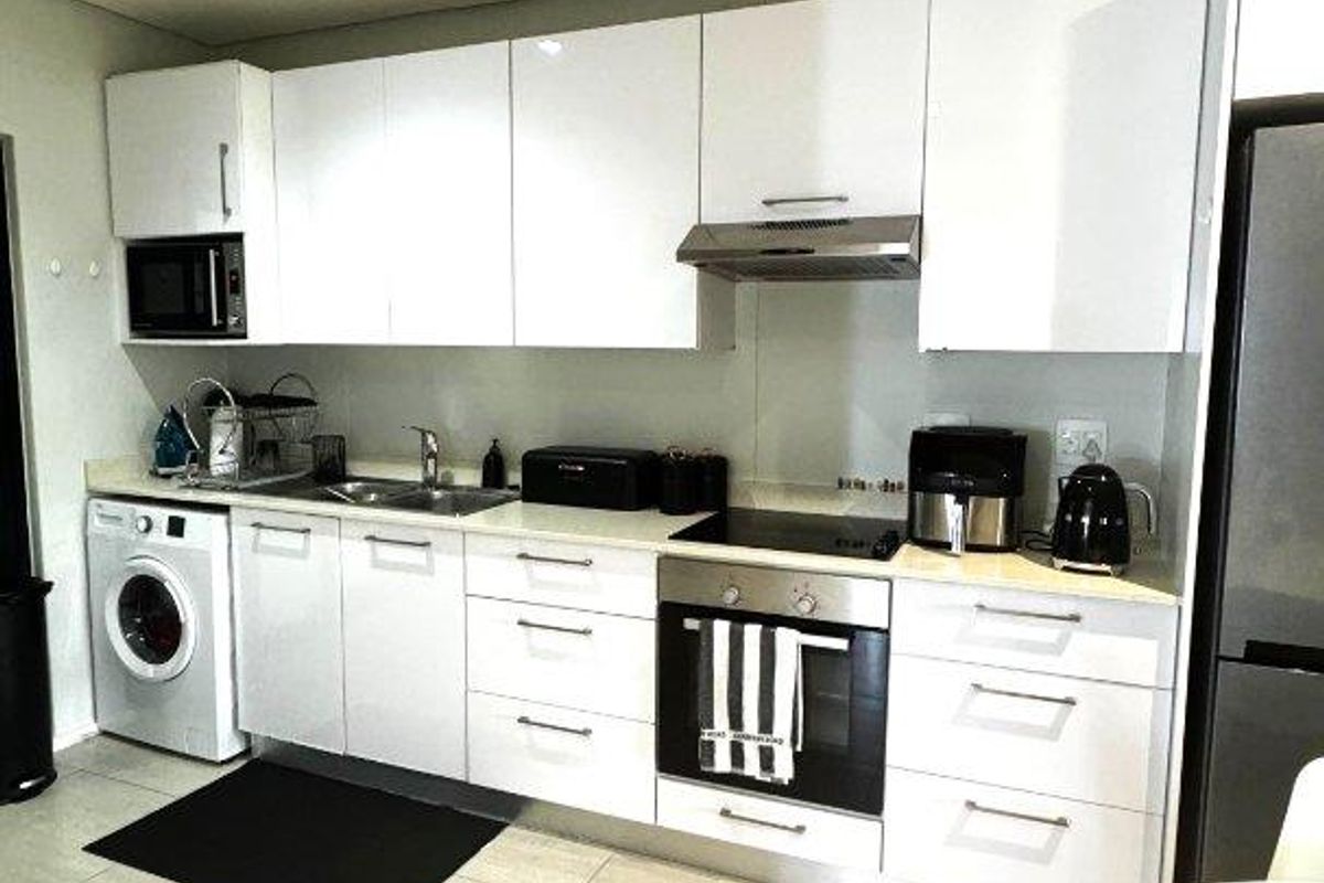 Modern kitchen featuring white cabinetry, integrated oven, hob, extractor fan, and built-in laundry appliance space with tiled flooring.