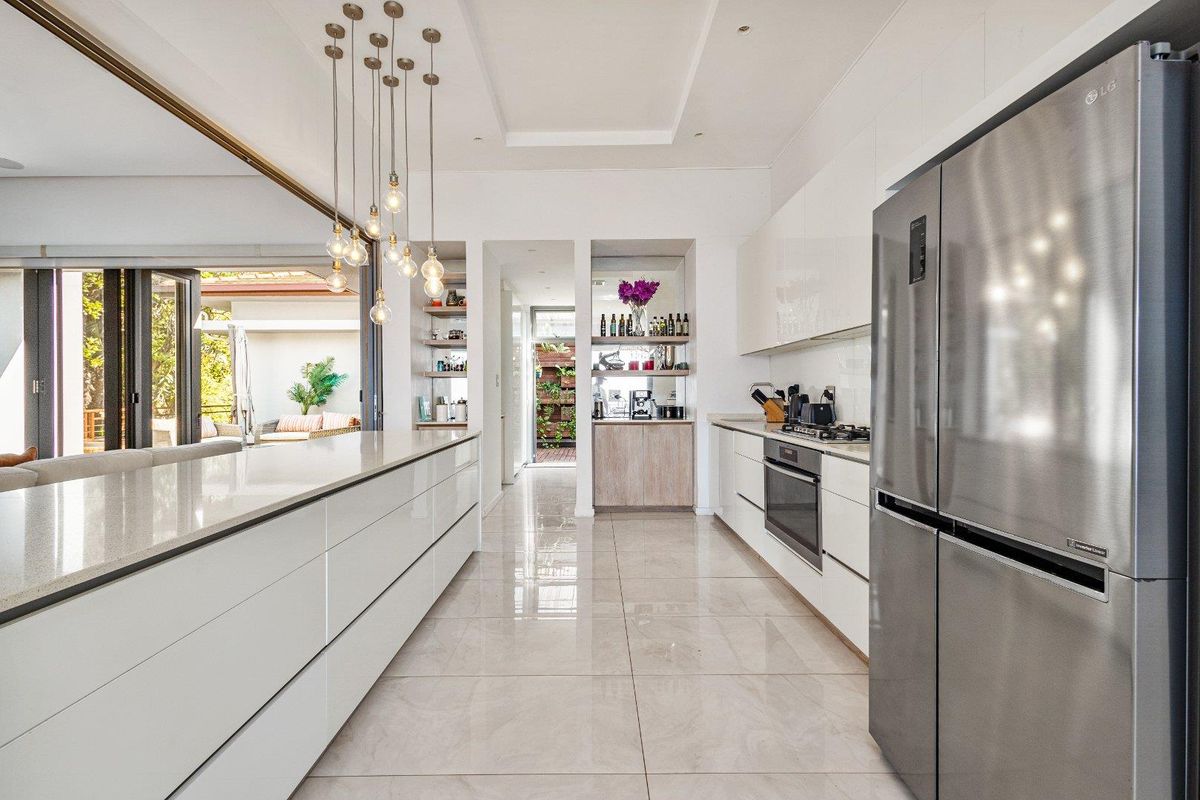 Modern kitchen featuring a large central island, sleek white cabinetry, integrated oven, gas hob, and polished tile flooring, flowing seamlessly into the outdoor patio area.