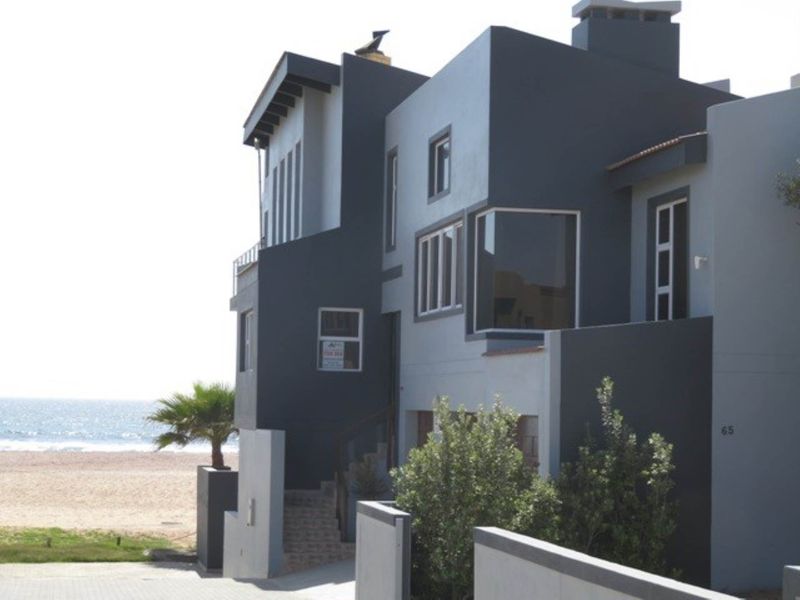 A modern multi-level beachfront property featuring a striking dark and light grey facade, bay windows, and direct access to the coastal area.