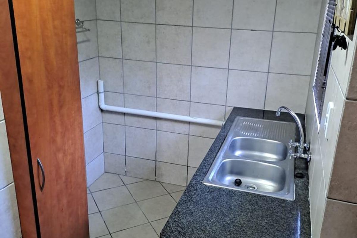 A functional laundry area featuring a stainless steel double sink, granite countertop, built-in cabinetry, and full-height ceramic wall tiling.