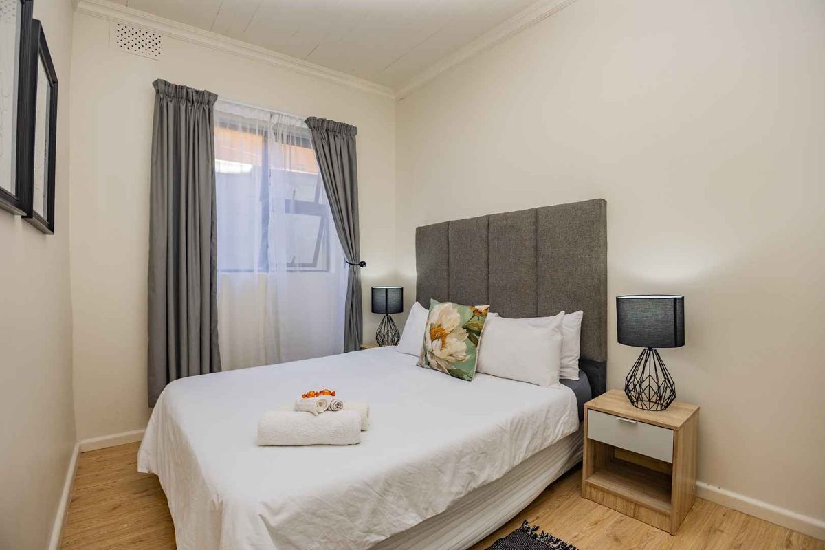A well-maintained bedroom featuring light wood-look flooring, neutral walls, and a window with curtain treatments.