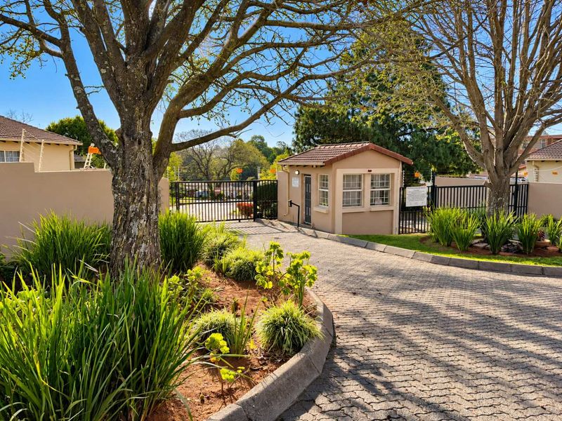 The entrance to the townhouse complex features a paved driveway, a secure guard house, and well-maintained landscaped gardens with perimeter security fencing.