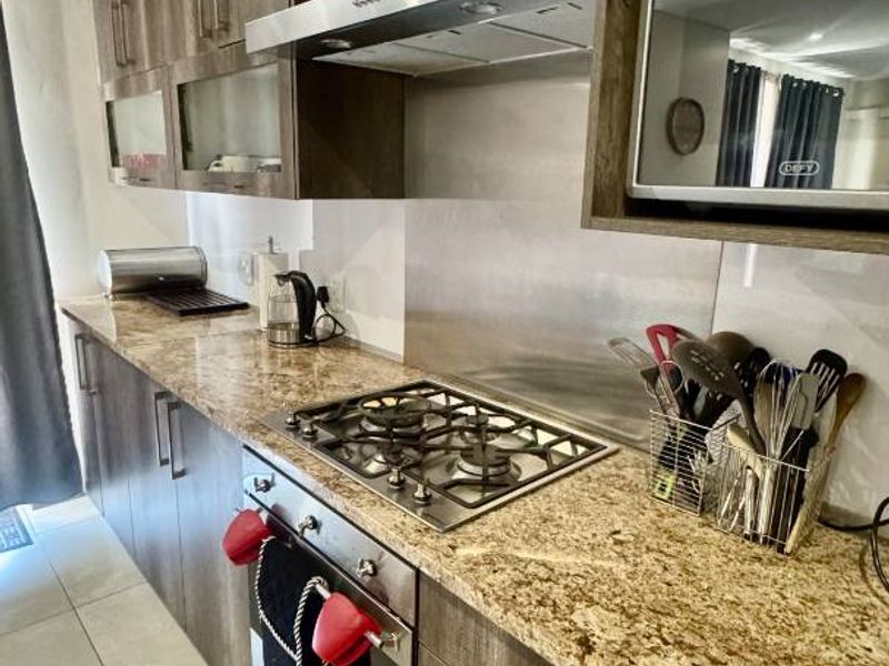 Modern kitchen featuring granite countertops, dark wood-finish cabinetry, built-in oven, gas hob, and stainless steel extractor fan.