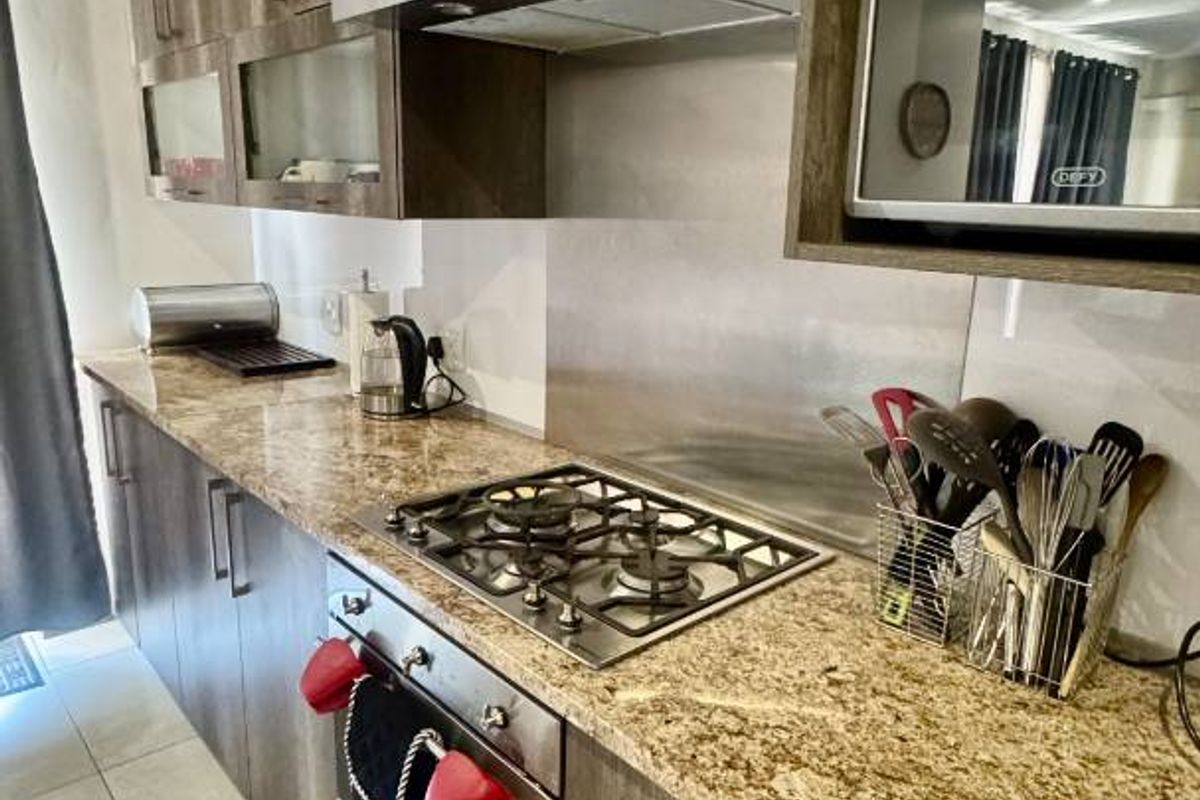 Modern kitchen featuring granite countertops, dark wood-finish cabinetry, built-in oven, gas hob, and stainless steel extractor fan.