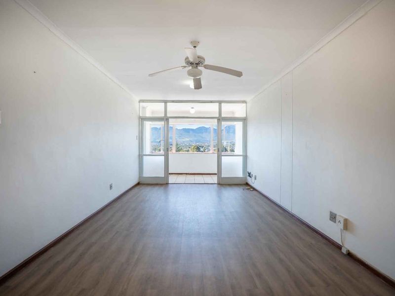 An empty, well-lit living room featuring laminate flooring, a ceiling fan, and direct access to a balcony with mountain views.