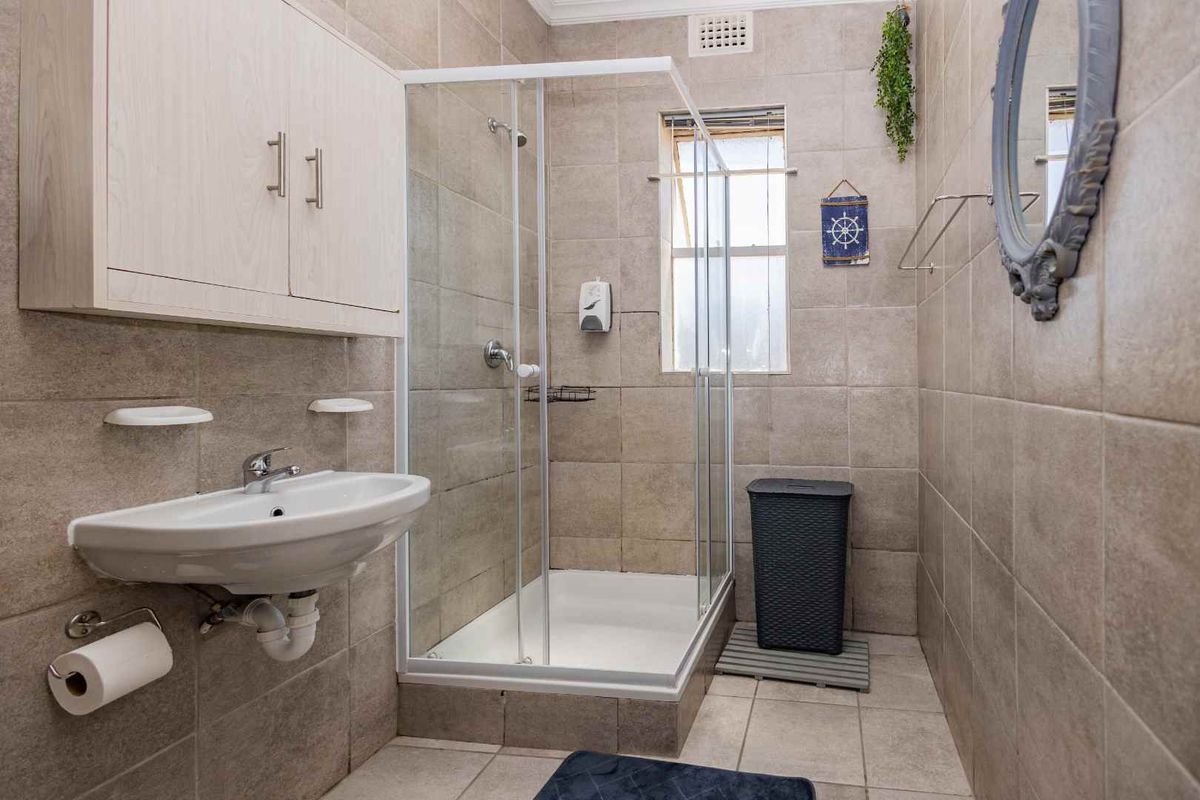A functional bathroom featuring a glass-enclosed shower, wall-mounted basin, and neutral floor-to-ceiling tiling.