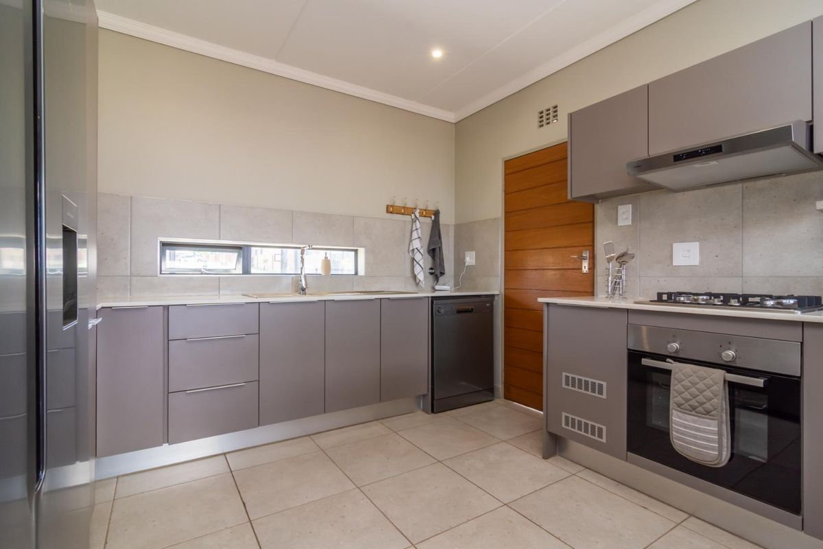 Modern kitchen featuring sleek grey cabinetry, stone countertops, built-in oven with gas hob, extractor fan, and neutral tiled flooring.