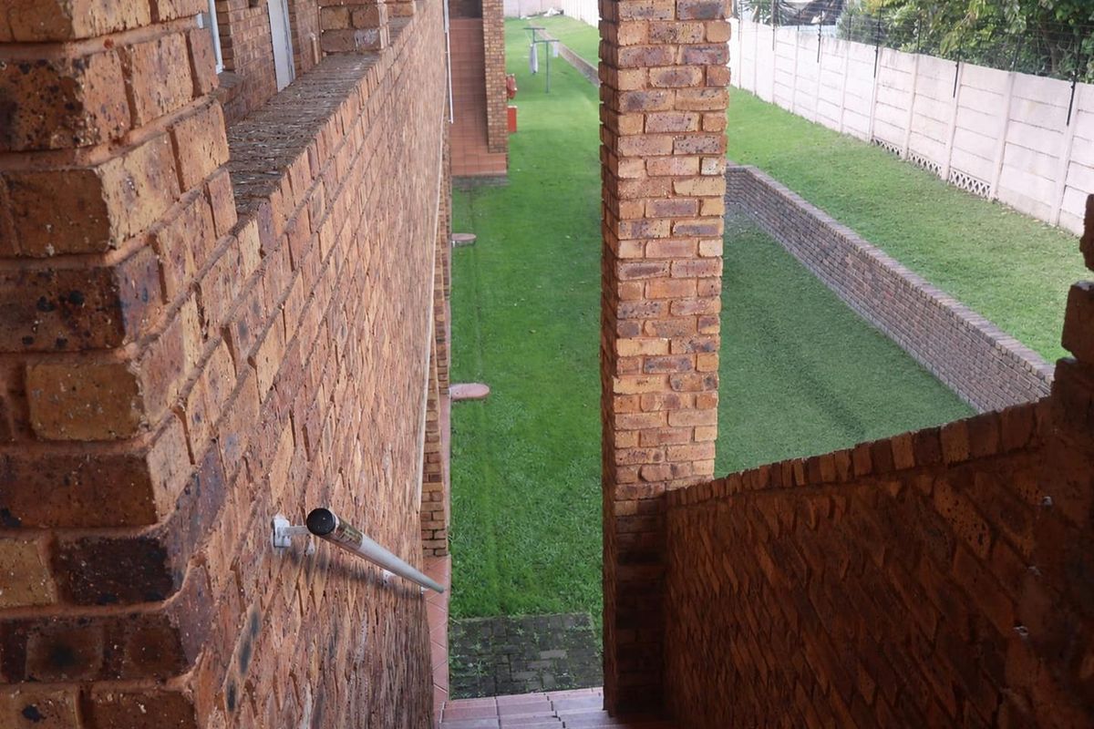 Exterior view of a brick staircase leading down to a communal garden area with a retaining wall and perimeter fencing.