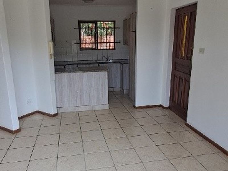 An empty open-plan living and kitchen area featuring tiled flooring, built-in cabinetry, and a functional kitchen layout with security bars on the window.