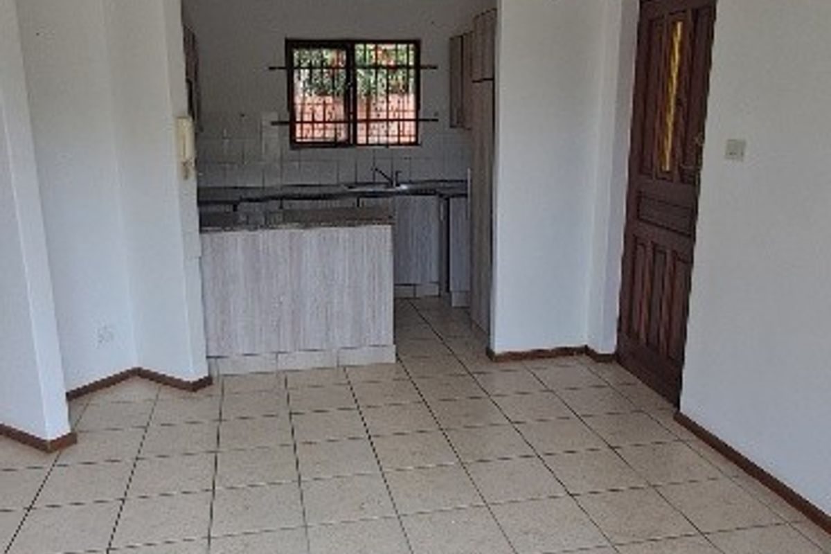 An empty open-plan living and kitchen area featuring tiled flooring, built-in cabinetry, and a functional kitchen layout with security bars on the window.