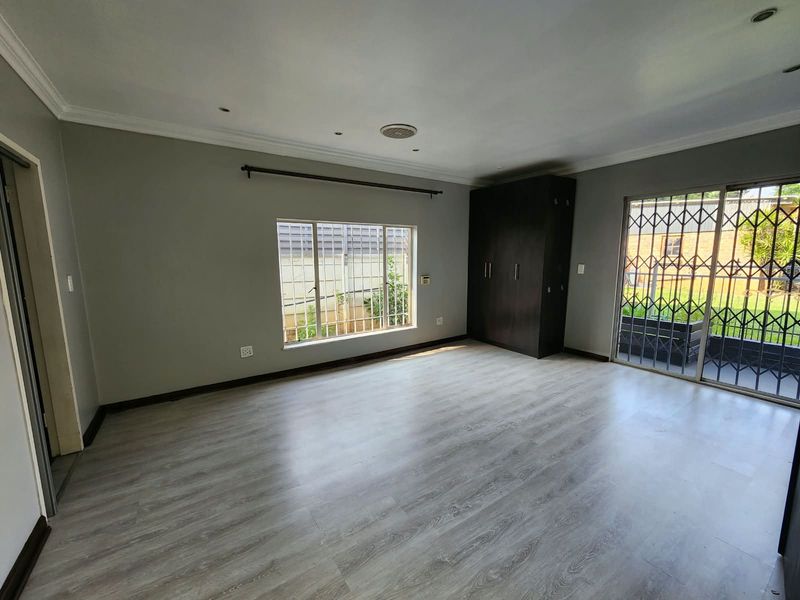 Spacious bedroom featuring modern laminate flooring, built-in wardrobe, and sliding glass doors with security gates leading to the exterior.