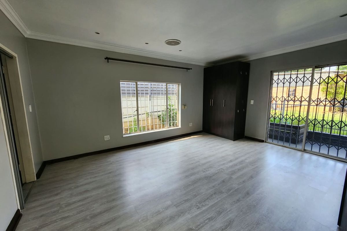 Spacious bedroom featuring modern laminate flooring, built-in wardrobe, and sliding glass doors with security gates leading to the exterior.