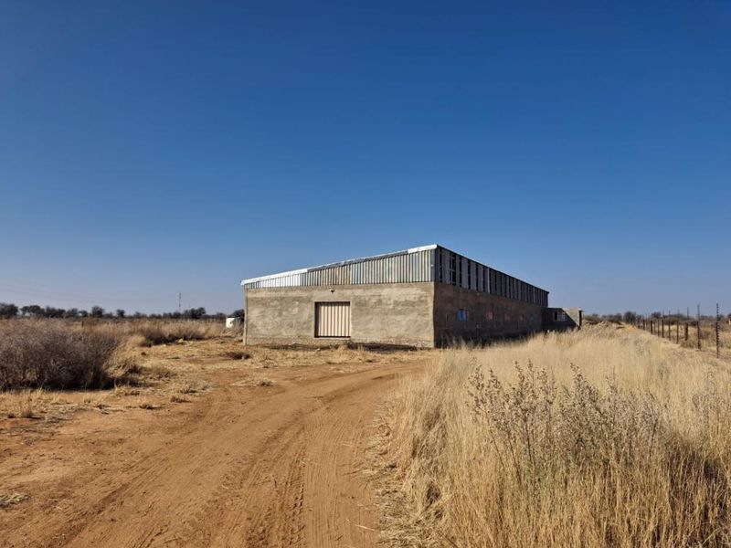 A large industrial-style outbuilding on a small holding, featuring concrete block construction, a corrugated metal roof, and perimeter electric fencing.