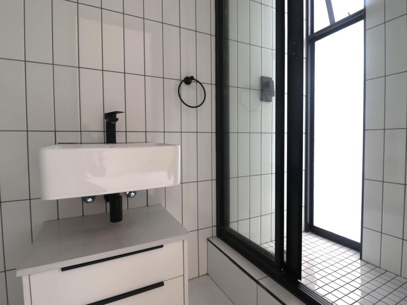 Modern bathroom featuring a wall-mounted basin with black tapware, tiled walls, and a glass-enclosed shower area with a clean, contemporary aesthetic.