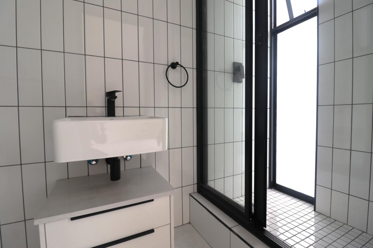 Modern bathroom featuring a wall-mounted basin with black tapware, tiled walls, and a glass-enclosed shower area with a clean, contemporary aesthetic.