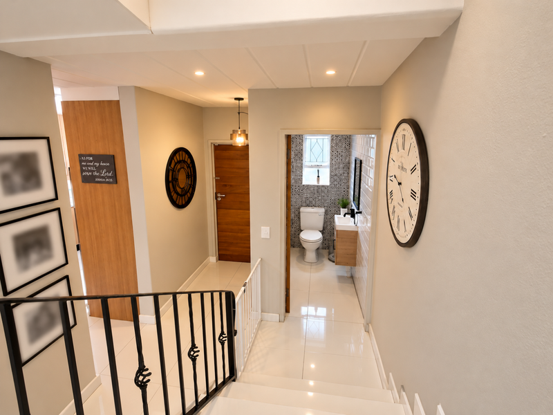 A bright hallway featuring tiled flooring, a wrought iron balustrade, and direct access to a modern bathroom with patterned wall tiles.