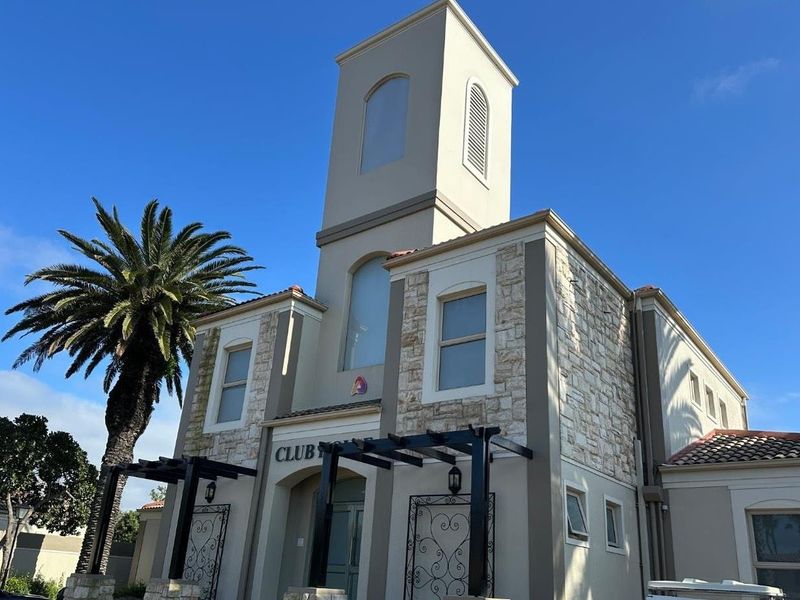 Exterior view of the apartment complex clubhouse featuring stone cladding, a prominent tower, and a decorative pergola entrance.