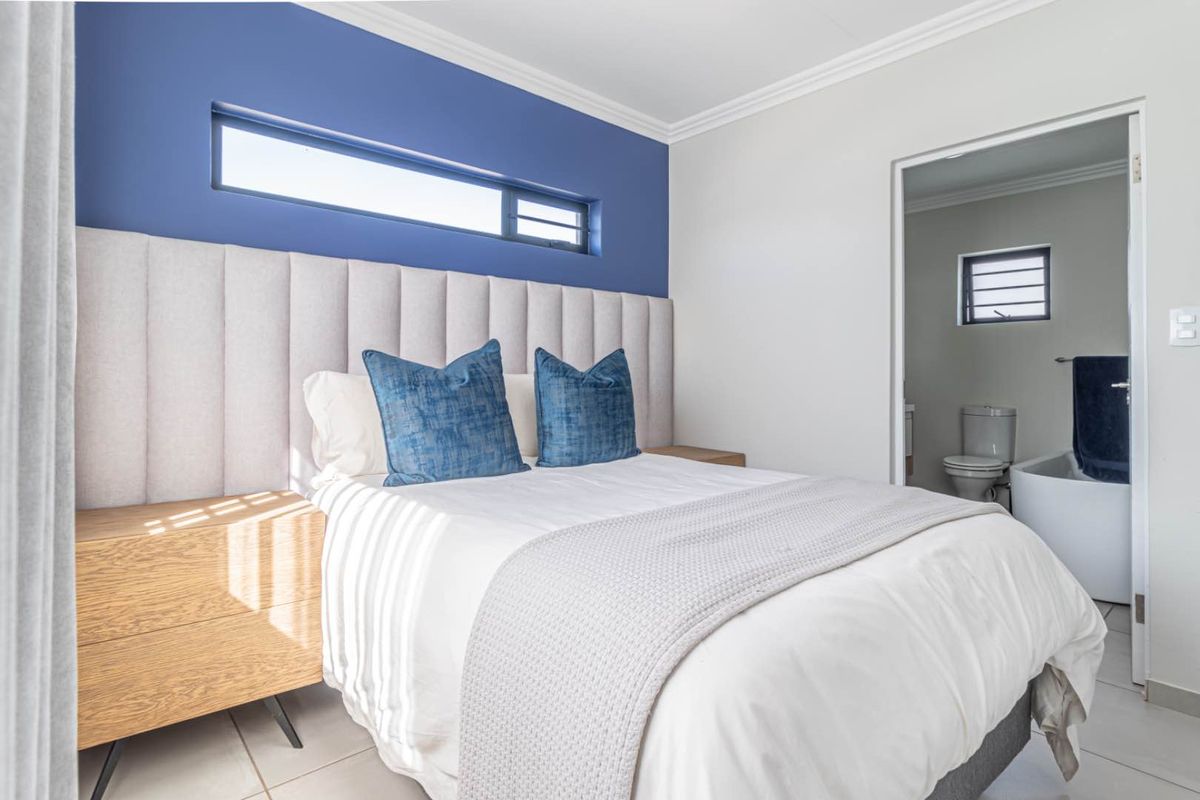 A well-maintained bedroom featuring a built-in upholstered headboard, accent wall, and an adjoining en-suite bathroom with modern fixtures.