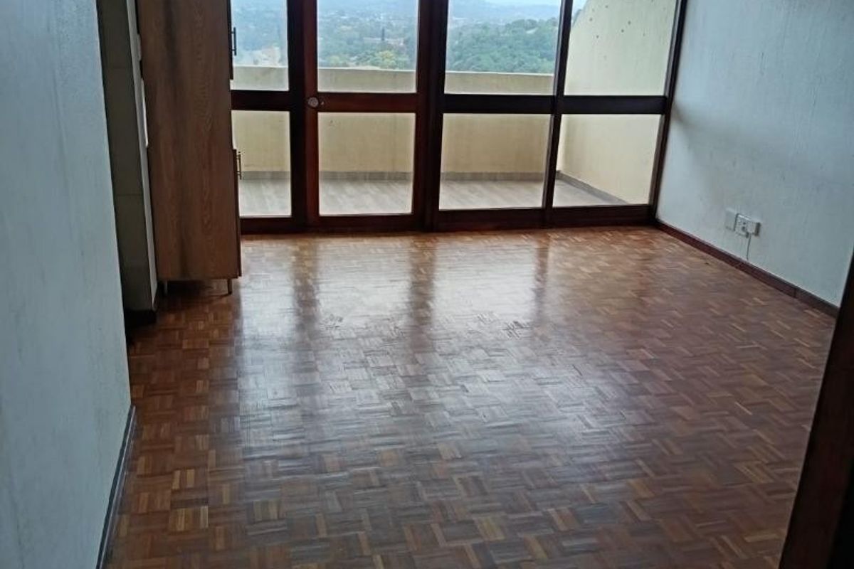 Bright, empty living area featuring classic parquet flooring and large glass doors providing natural light and direct access to an outdoor balcony.