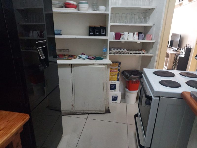 A functional kitchen area featuring built-in cabinetry, open shelving for storage, and tiled flooring, requiring cosmetic updates to improve its overall aesthetic.
