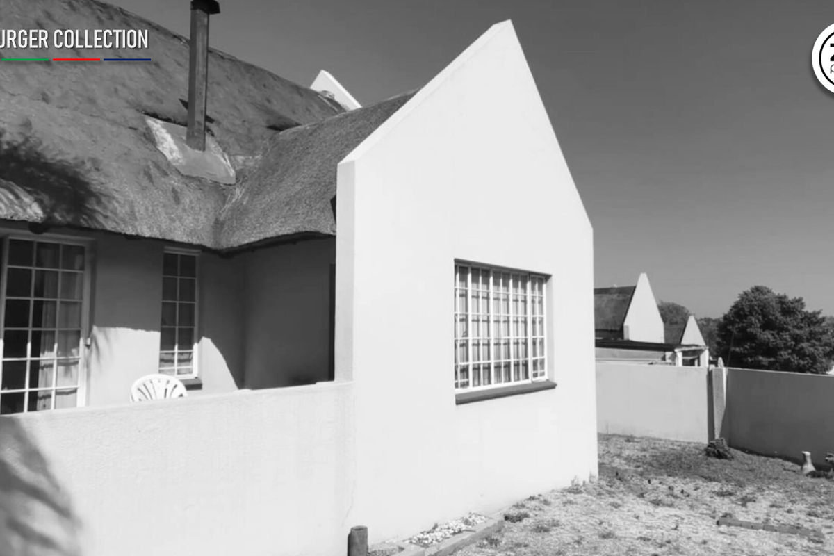 Rear view of a house featuring a traditional thatch roof, security bars on windows, and a surrounding boundary wall.