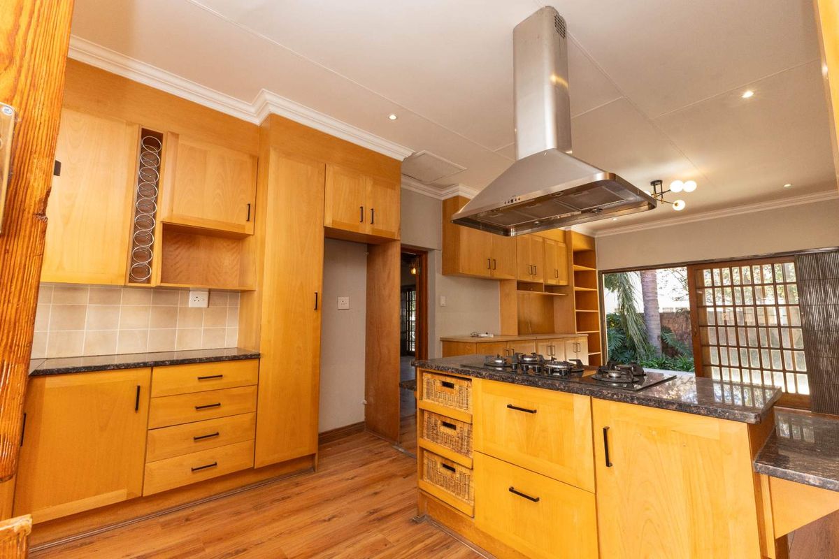 A functional kitchen featuring light wood cabinetry, granite countertops, a central island with a built-in gas hob, and a stainless steel extractor fan.