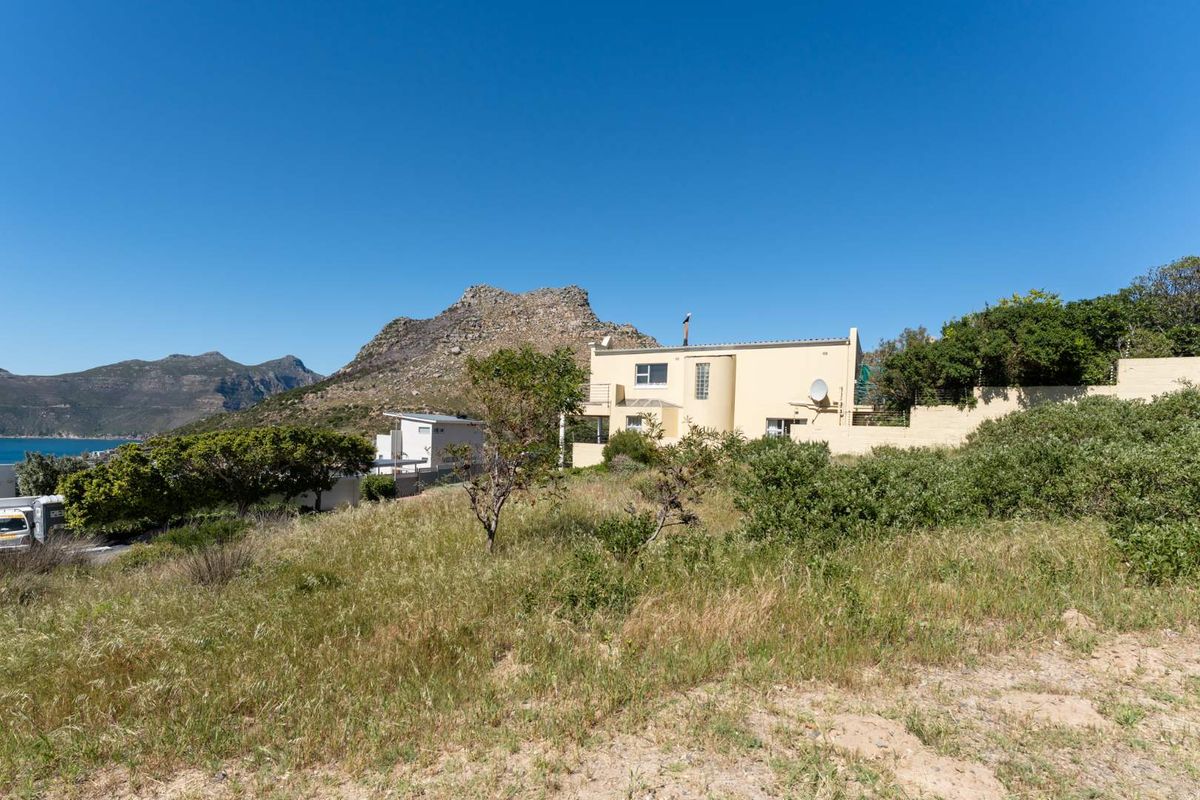 Rear view of the residential property showing the building structure, boundary walls, and surrounding natural landscape with mountain views.